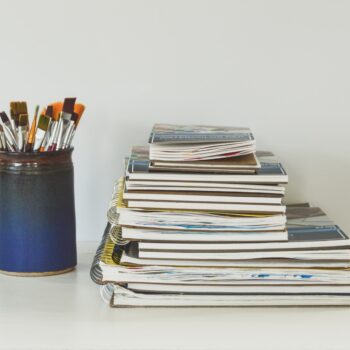 Marketing Image of a pile of art books next to a tin of brushes